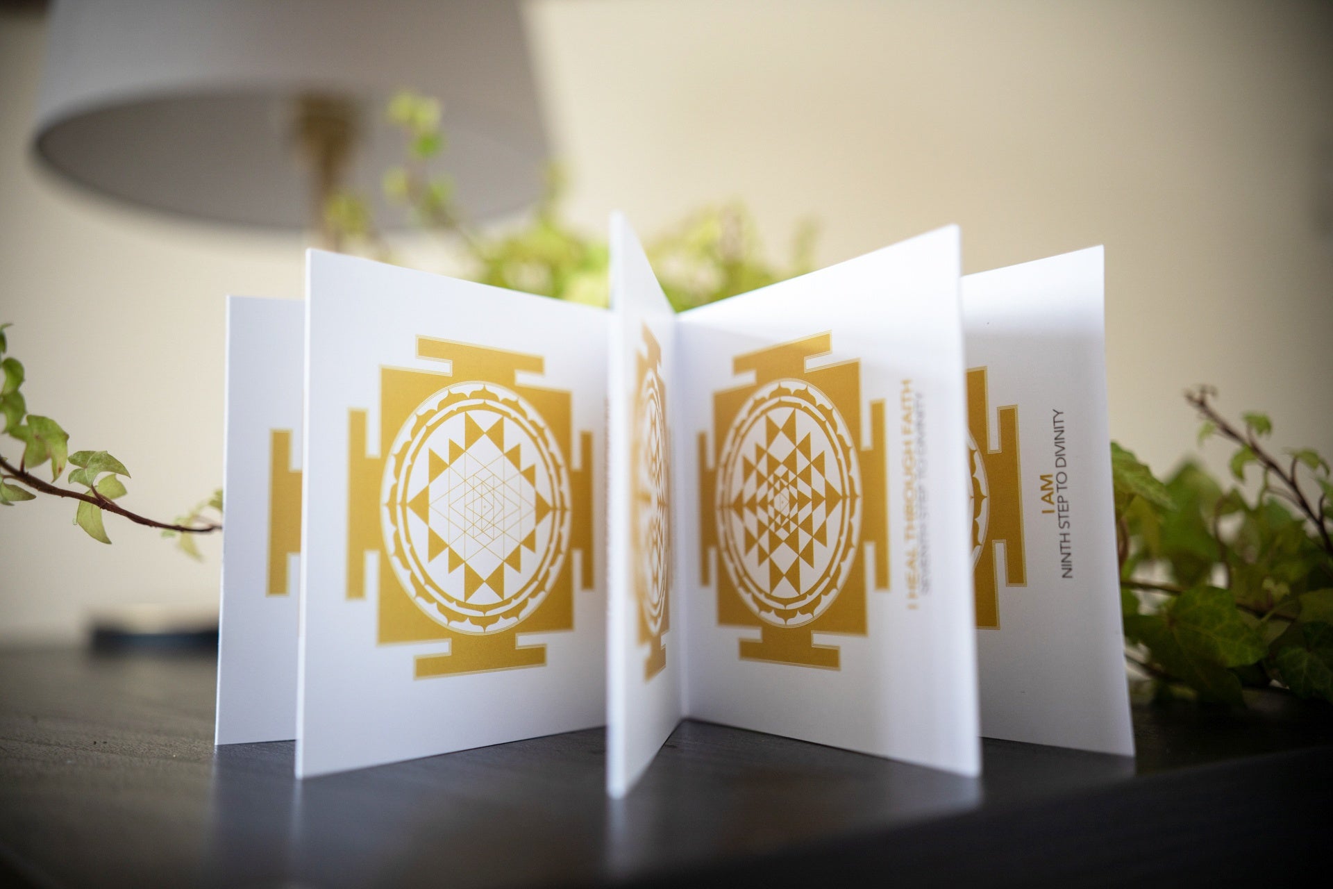 Small accordion booklet open on wooden altar surface beside oil lamp and flowers - Bhakti Shop
