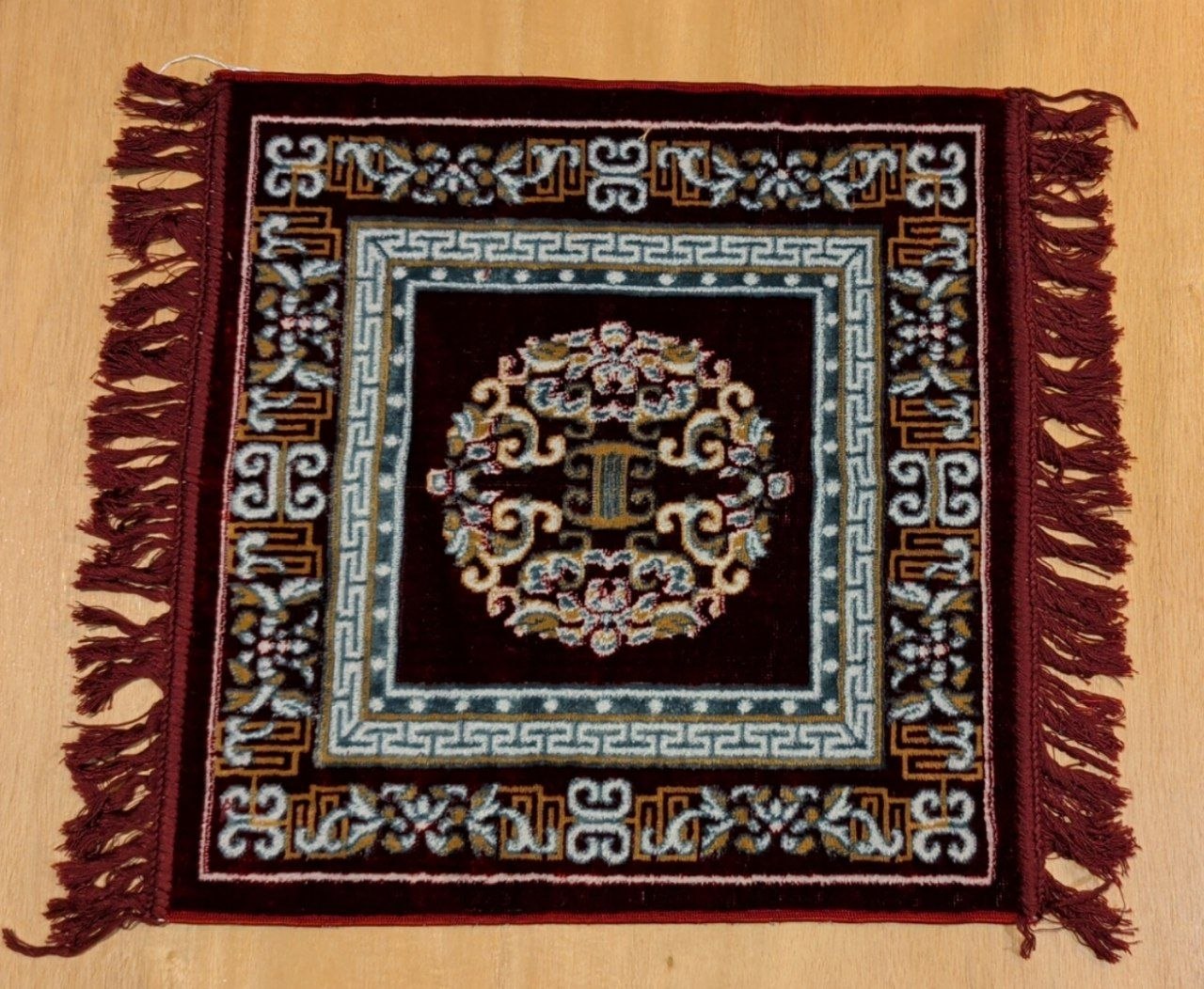Close-up of meditation carpet showing teal floral medallion, geometric meander border, and deep red field - Bhakti Shop